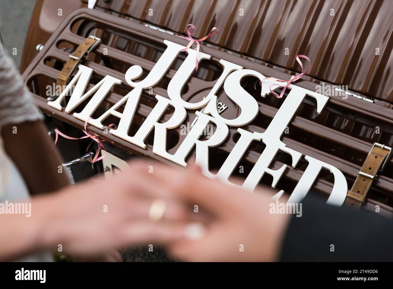 Le mani con gli anelli degli sposi sposi sullo sfondo di un'auto d'epoca con un cartello "Just Married". Il primo piano richiama l'attenzione sugli anelli e. Foto Stock