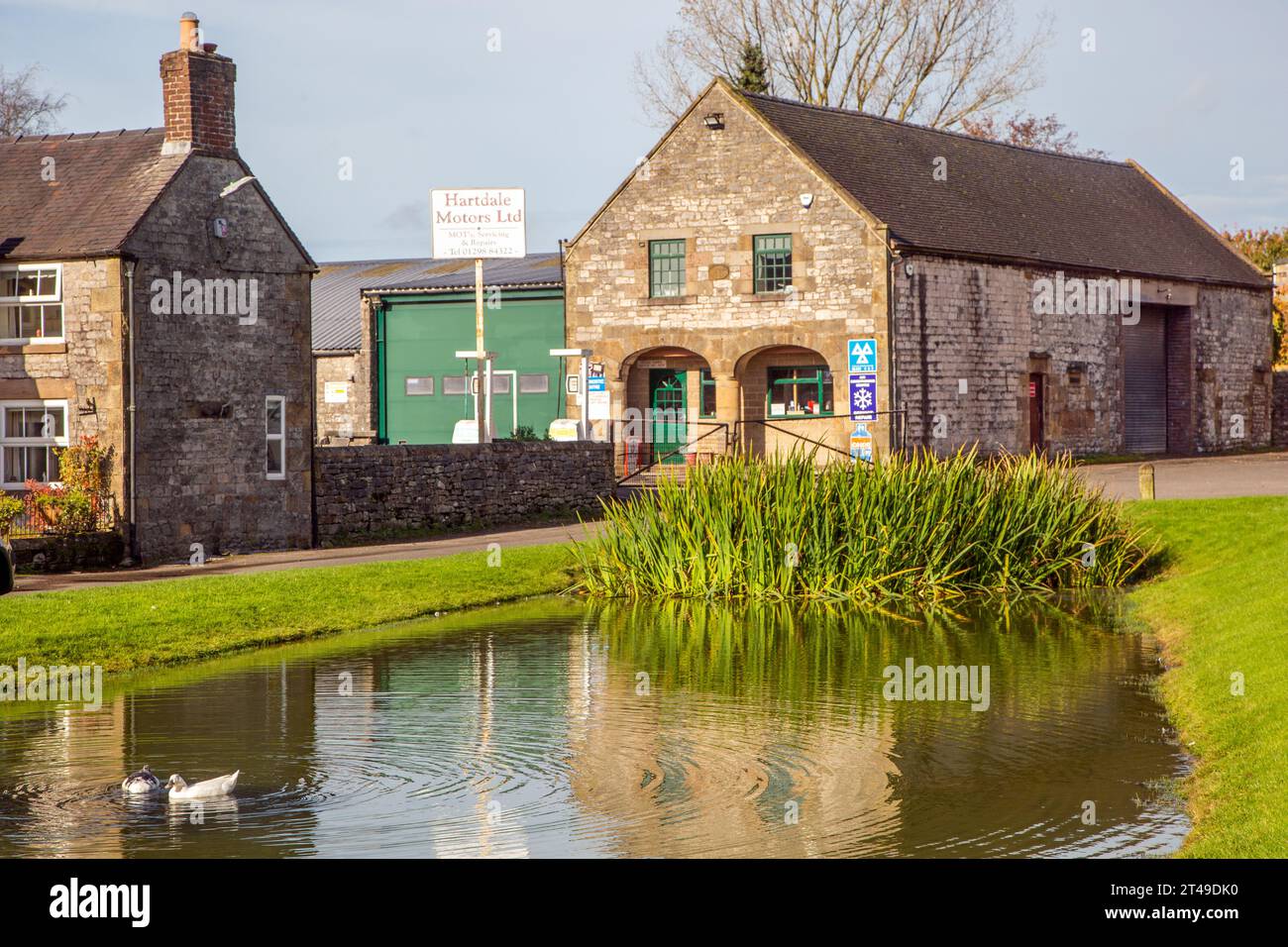Lo stagno delle anatre del villaggio e il garage nel villaggio del Derbyshire Peak District di Hartington, Inghilterra, Regno Unito Foto Stock