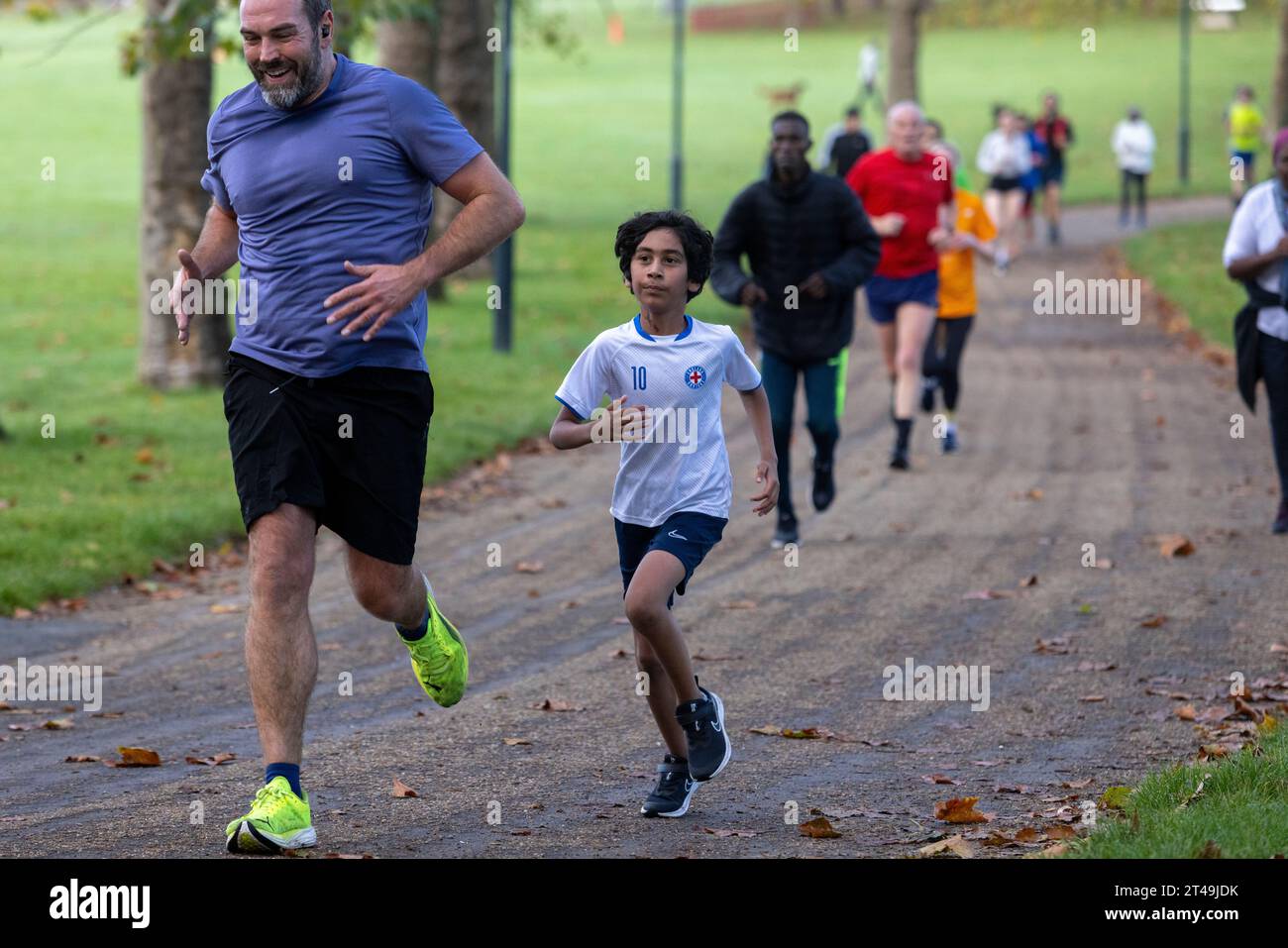 Gladstone Park, Parkrun, Dollis Hill, North West London. Un ragazzo con una camicia inglese che corre al fianco di un uomo di mezza età. Foto Stock