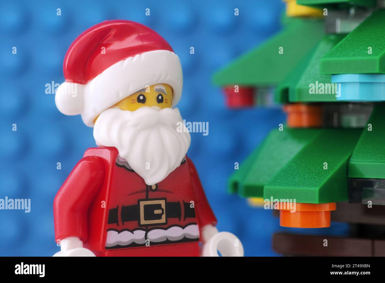 Tambov, Federazione Russa - 29 ottobre 2023 Una minifigura Lego Babbo Natale in piedi accanto a un albero di Natale sullo sfondo di una base blu Foto Stock