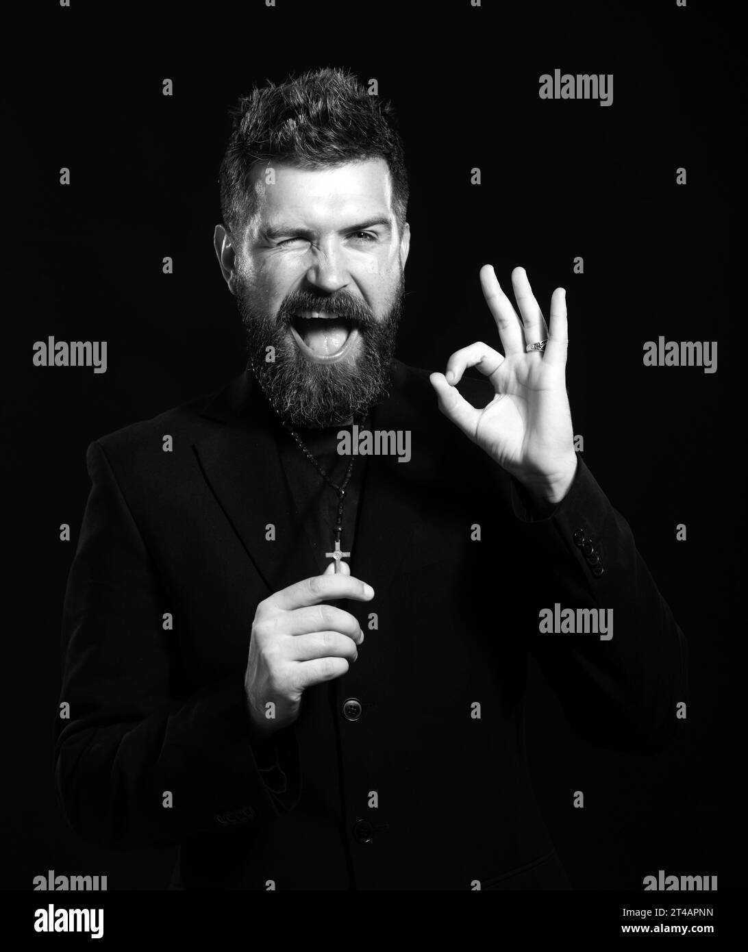 Giovane uomo che indossa uniforme prete in piedi su sfondo bianco facendo un gesto ok con mano sorridente, occhio guardando attraverso le dita con volto felice. Foto Stock