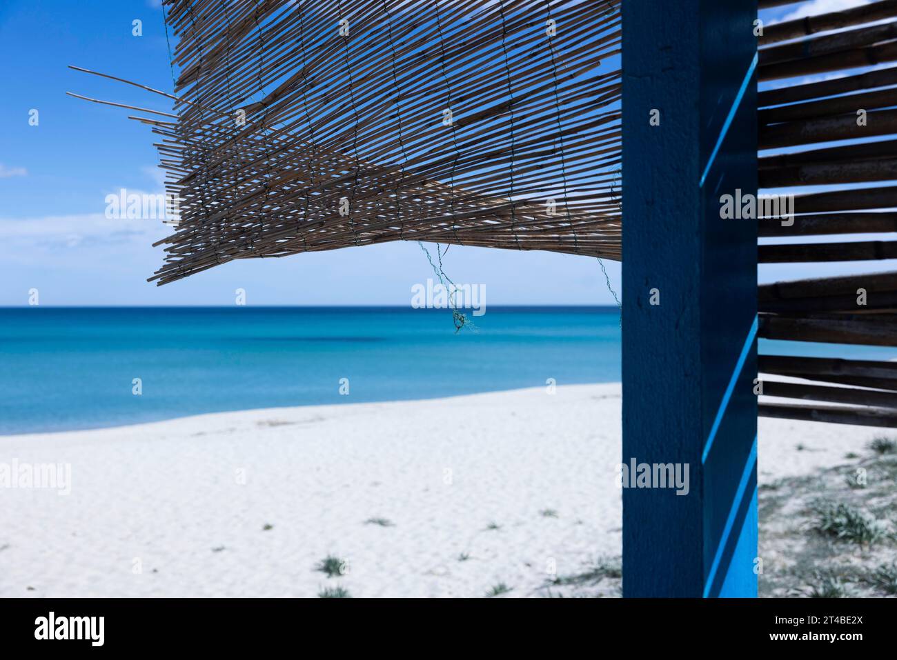 Tappeto di paglia appeso al vento su una capanna su una spiaggia di sabbia bianca di fronte a un mare azzurro brillante, Ogliastra, Sardegna, Italia Foto Stock