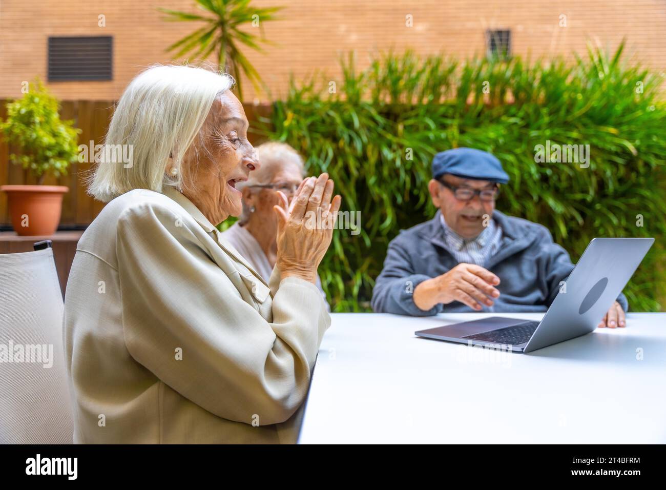 Persone anziane che sorridono e si divertono con il laptop in un geriatrico Foto Stock