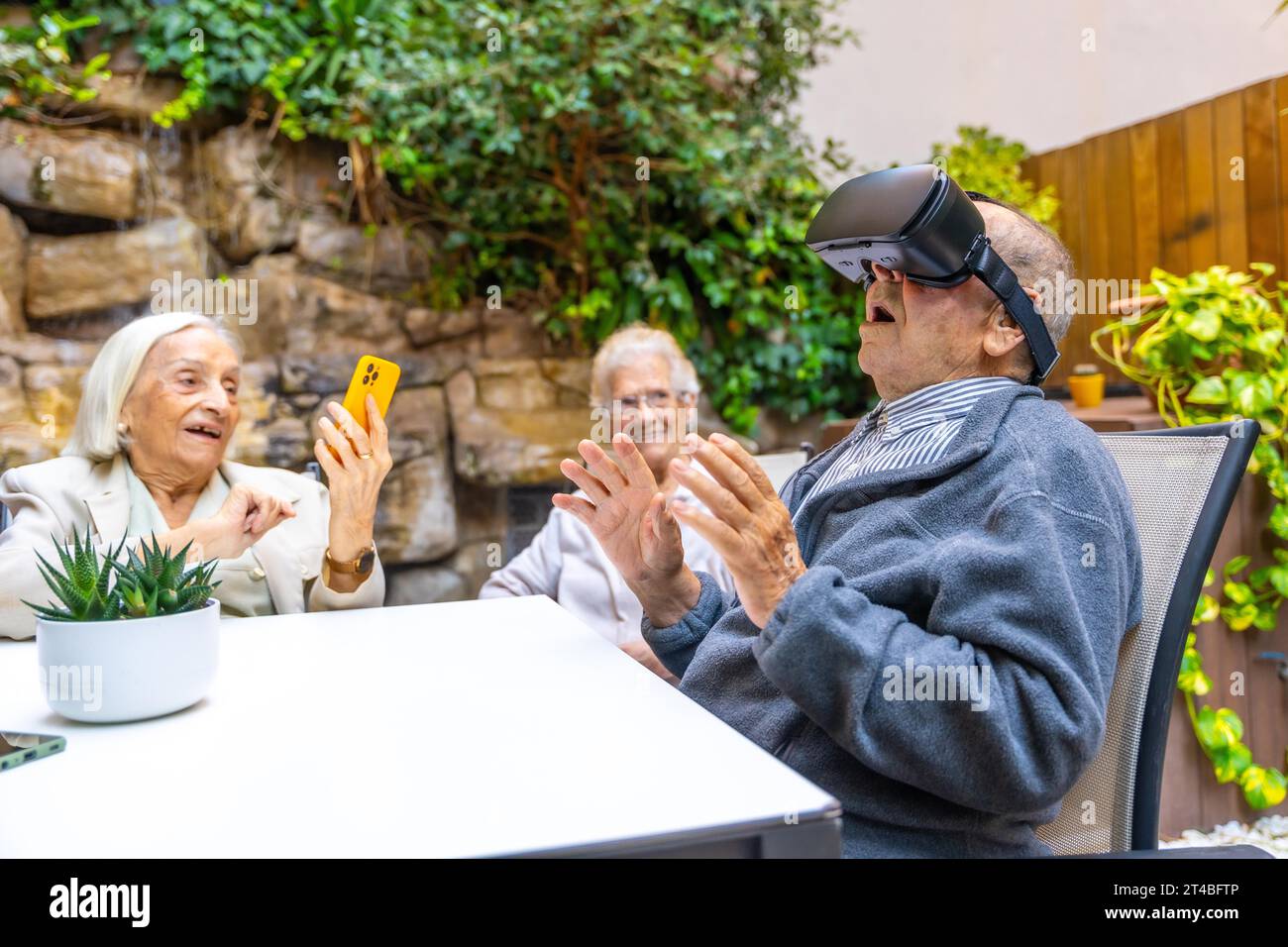 Uomo anziano che usa occhiali di realtà virtuale seduto sul giardino di una casa di cura Foto Stock