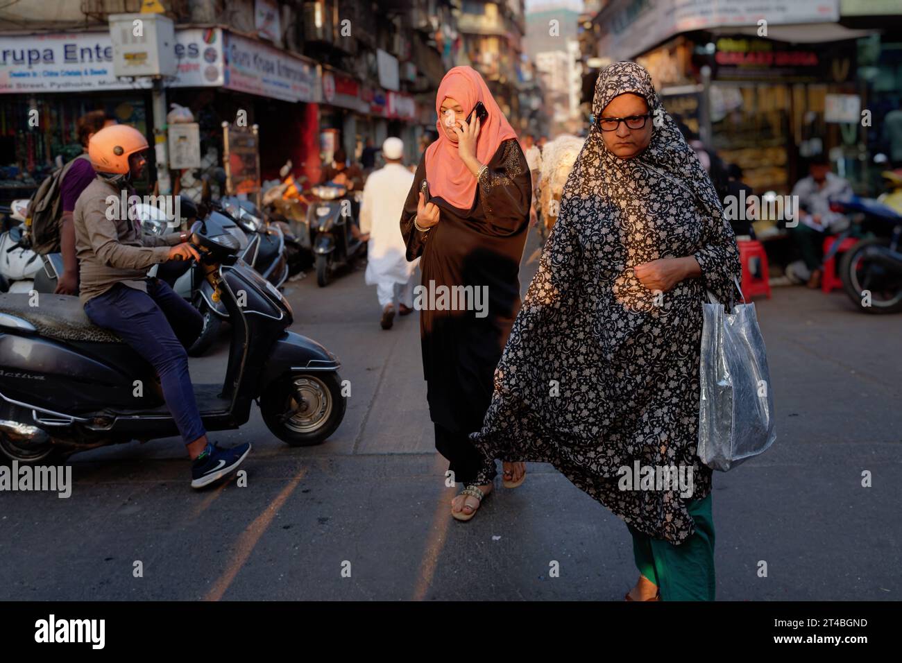 Due donne musulmane in abito islamico che attraversano la trafficata Kalbadevi Road, nella zona commerciale di Bhuleshwar, dominata dagli indù, a Mumbai, in India Foto Stock