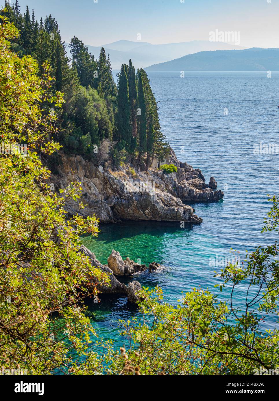 Promontorio roccioso con cipressi e mare turchese sulla costa nord-orientale delle Isole Ionie di Corfù, Grecia, guardando verso l'Albania Foto Stock
