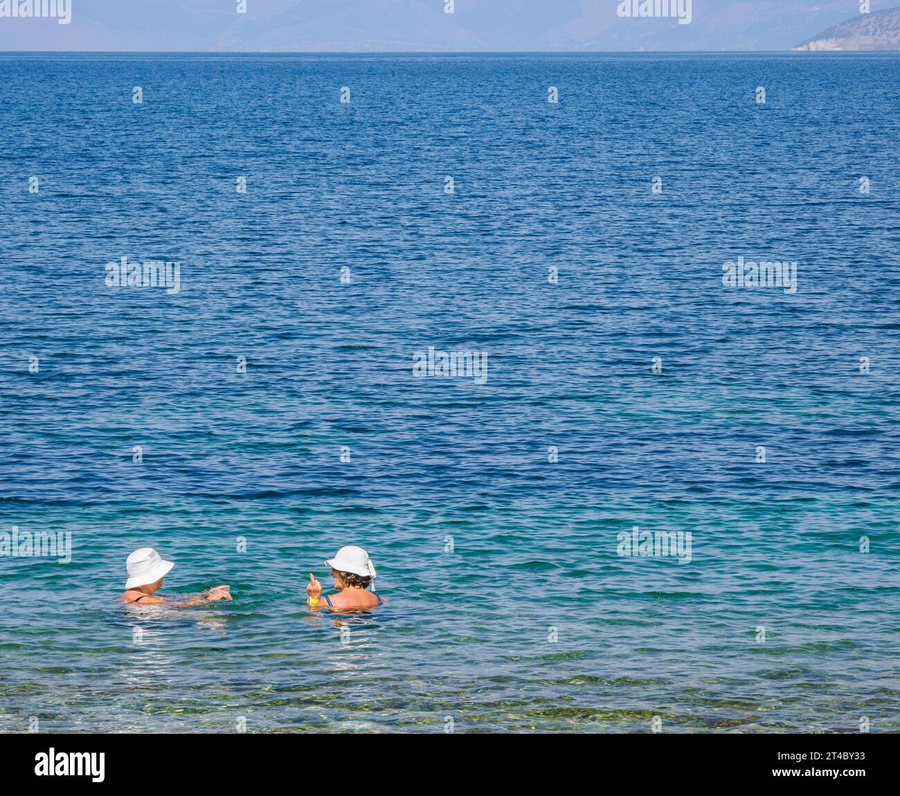 Due signore che indossano cappelli bianchi che chiacchierano in mare a Corfù, nelle Isole Ionie della Grecia Foto Stock