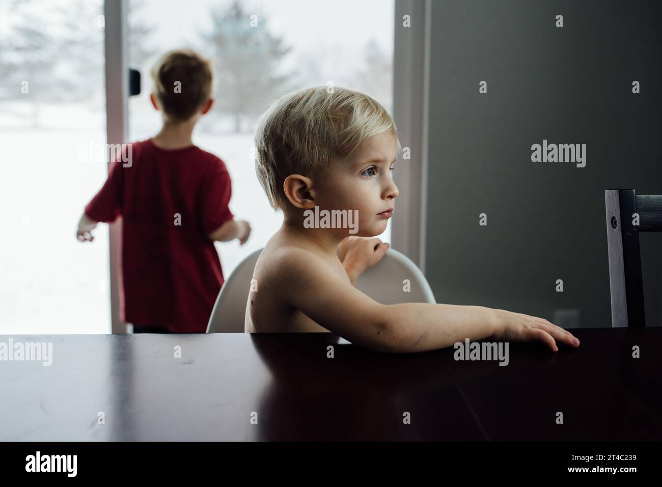 Il bambino biondo guarda lontano dalla fotocamera mentre è seduto a te Foto Stock