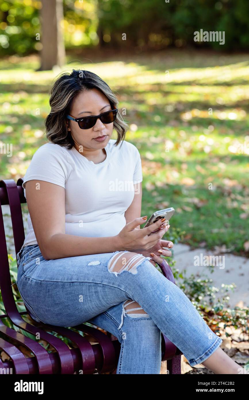 Immagine verticale di una donna che indossa gli occhiali da sole e guarda il telefono Foto Stock