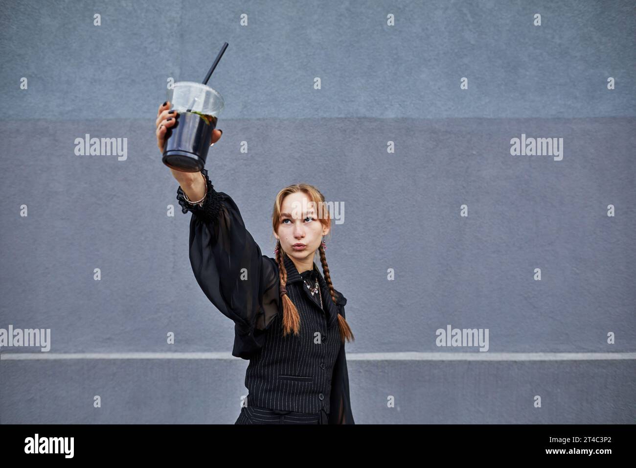 ragazza che fa un volto con un drink invece di un telefono Foto Stock