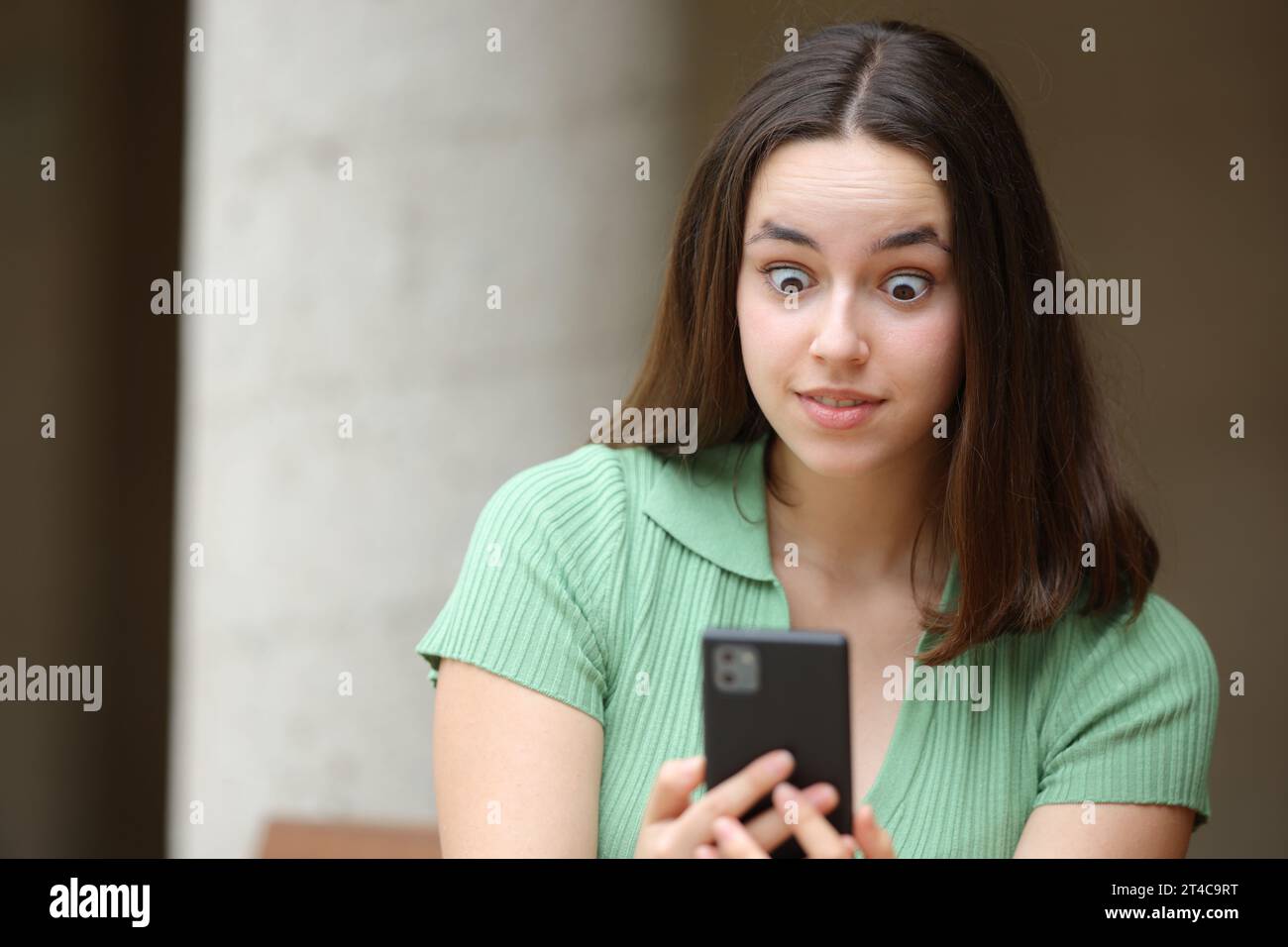 Ritratto frontale di una donna scioccata che controlla le notizie telefoniche per strada Foto Stock