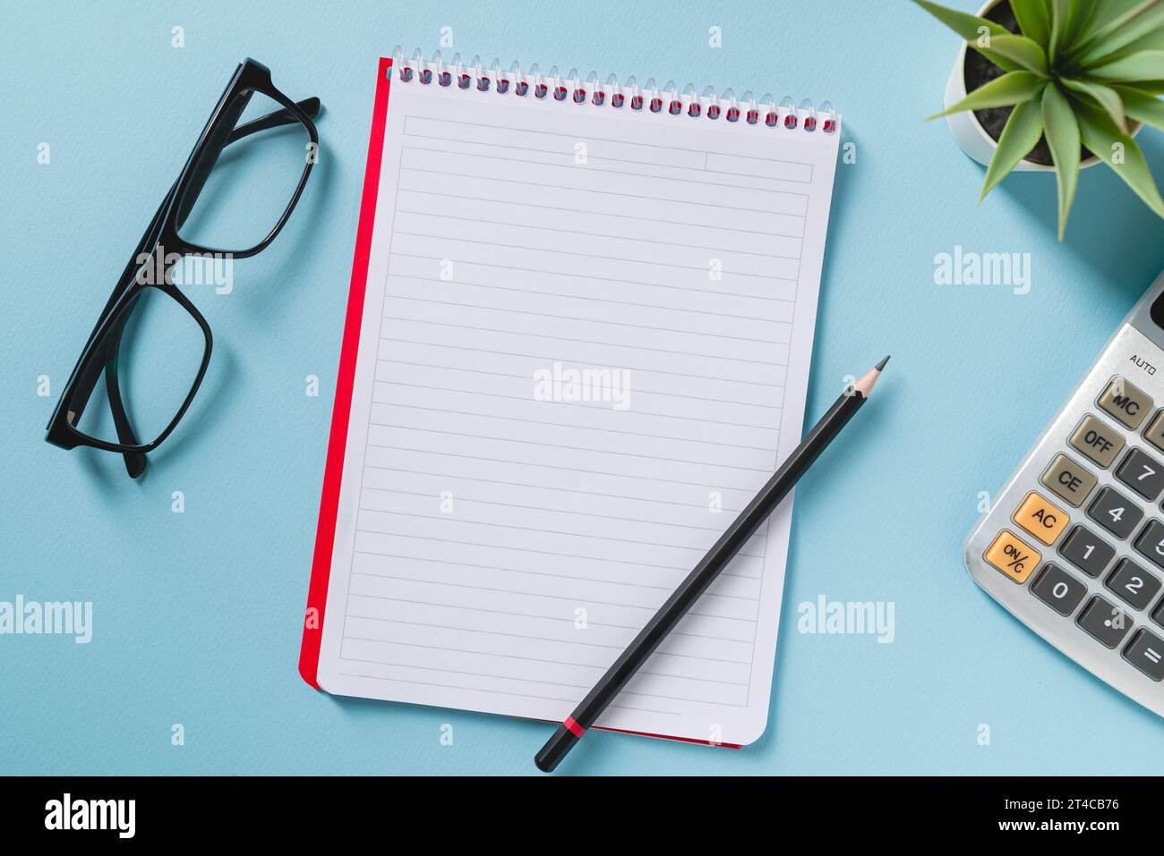Vista dall'alto di notebook vuoto, occhiali, penna, calcolatrice e pianta verde su una scrivania da ufficio blu Foto Stock