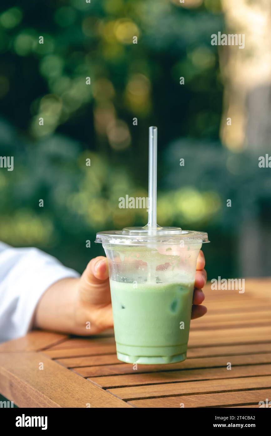 Latte matcha freddo in una tazza di plastica nelle mani di una donna. Foto Stock