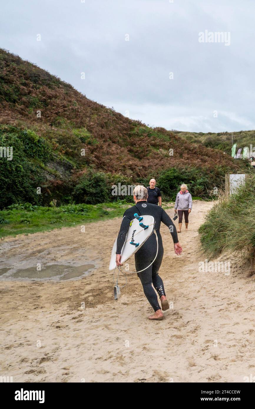 Un surfista che porta la sua tavola da surf e lascia Crantock Beach a Newquay in Cornovaglia, nel Regno Unito. Foto Stock
