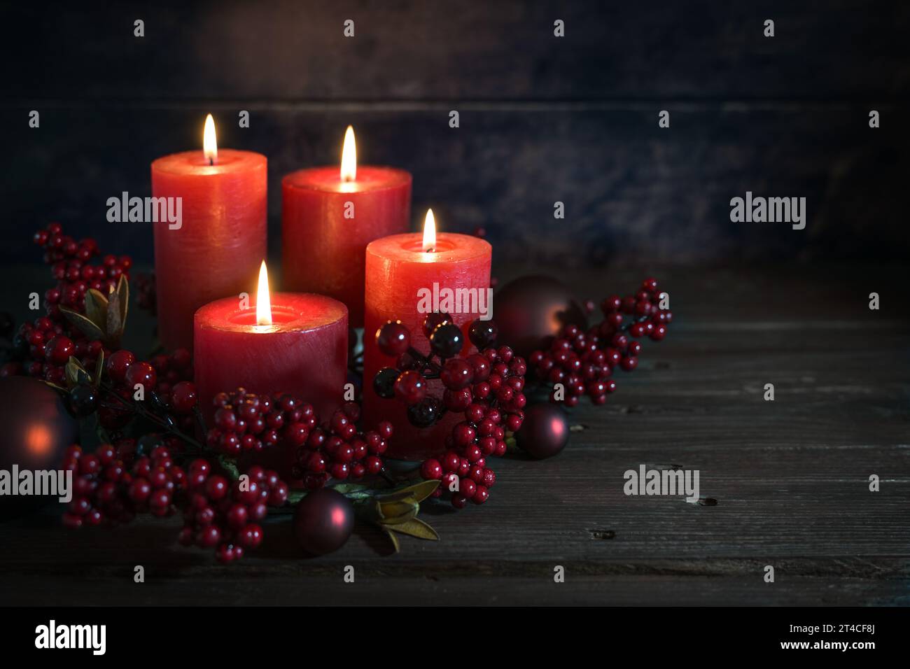 Decorazione dell'avvento in rosso scuro con candele accese, decorazione in berrie e palline di Natale su uno sfondo rustico in legno, spazio per la copia, messa a fuoco selezionata, Foto Stock