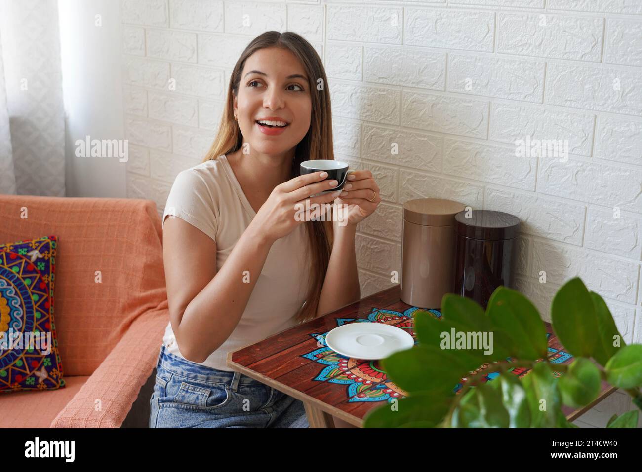 Annunci di caffè. Bella giovane donna che beve caffè a casa la mattina. Una giovane donna allegra prende il cappuccino nel suo accogliente appartamento. Foto Stock