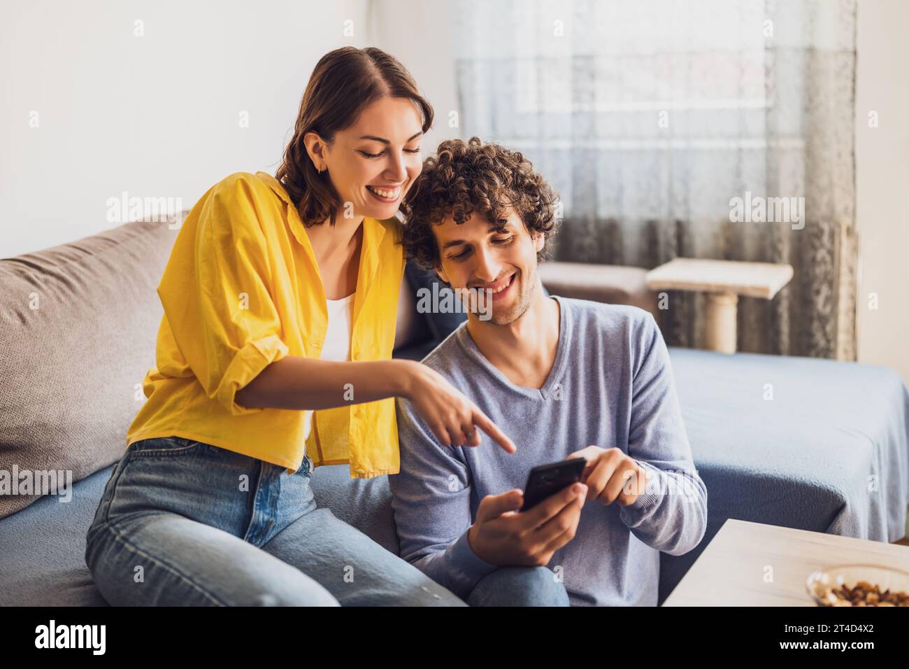 Ritratto di una giovane coppia felice che guarda lo smartphone a casa. Foto Stock