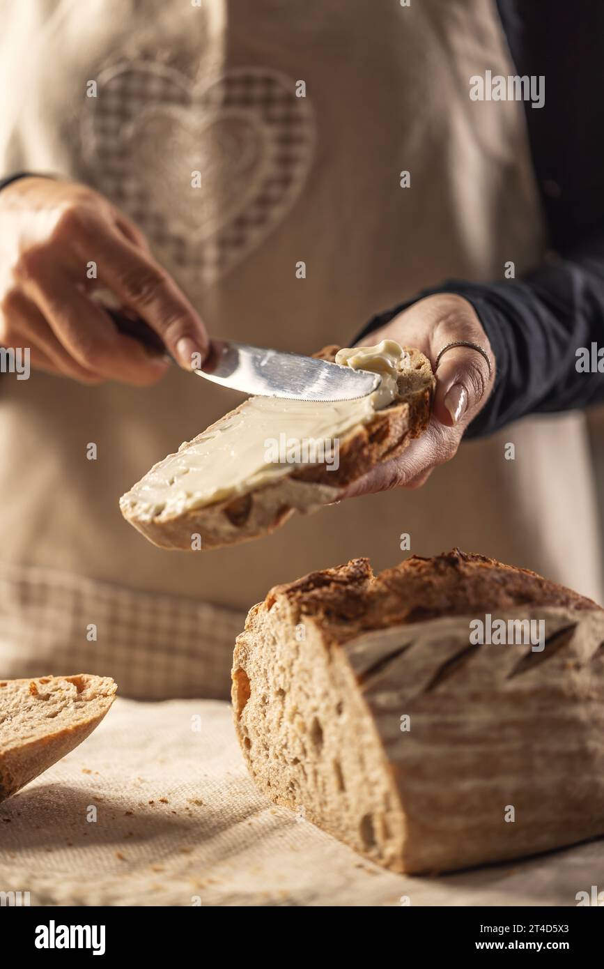 Una donna prepara del pane delizioso, spalma il formaggio con un coltello da posate - da vicino. Le donne spalmano il formaggio cremoso su una fetta di pane. Foto Stock