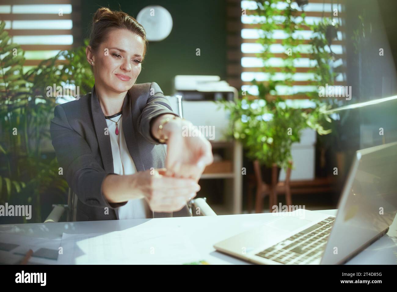 Ambiente di lavoro sostenibile. donna d'affari moderna sorridente in un moderno ufficio ecologico con un notebook che si allunga le mani. Foto Stock