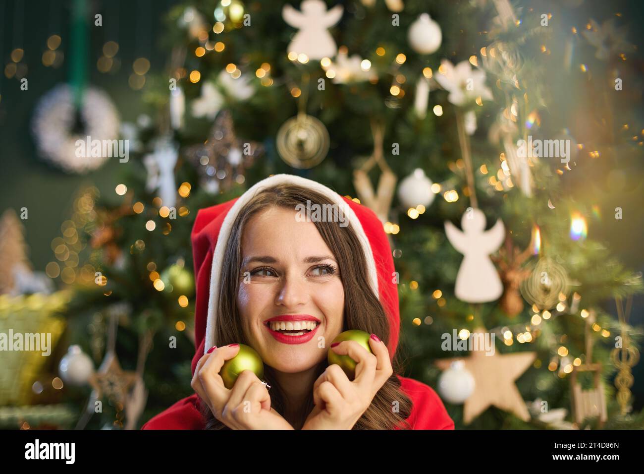 Natale. Elegante donna sorridente di 40 anni con ballo di Natale vicino all'albero di Natale nel moderno soggiorno. Foto Stock