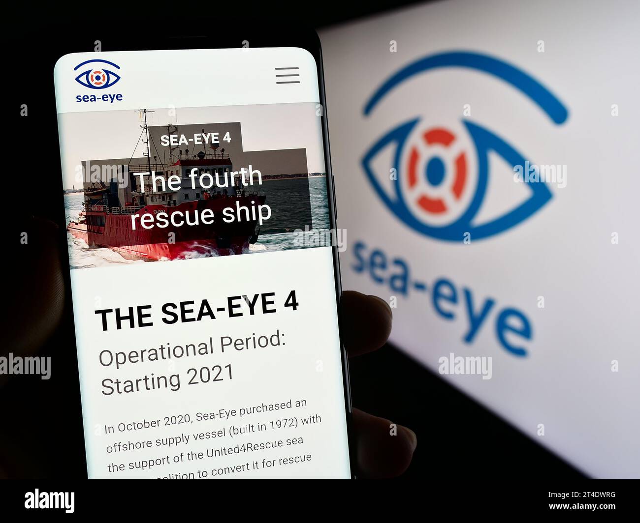 Persona che possiede uno smartphone con una pagina Web dell'associazione tedesca di soccorso marittimo Sea-Eye e.V. davanti al logo. Concentrarsi sul centro del display del telefono. Foto Stock