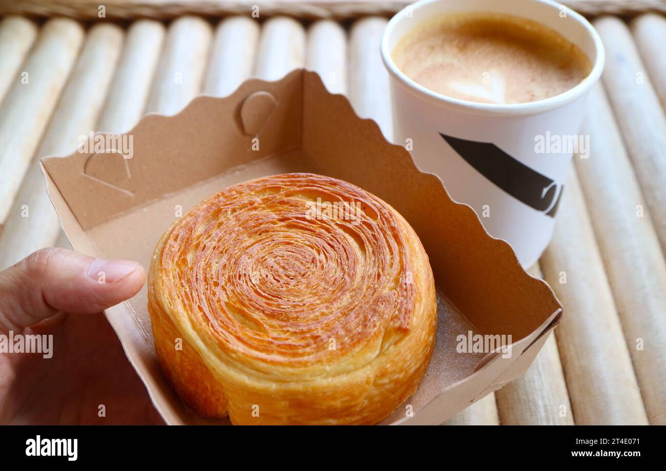 Mano che tiene una ciotola di carta di croissant supremo con caffè sfocato sullo sfondo Foto Stock