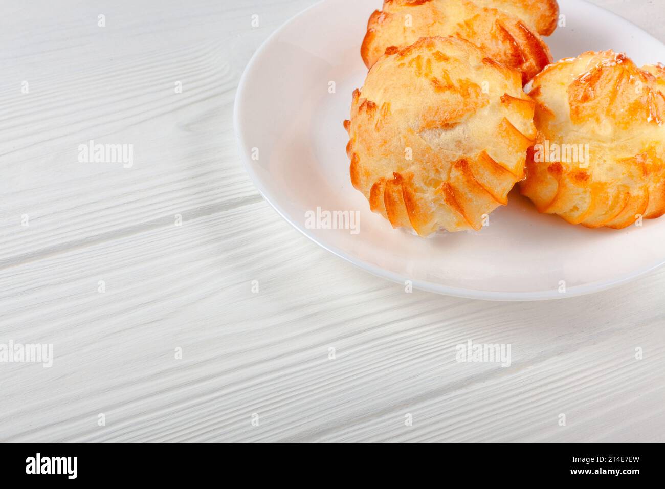 Profiterole dorate ripiene di panna, servite su un piatto bianco su un tavolo bianco da vicino. un delizioso abbinamento di dessert per ogni occasione. Foto Stock