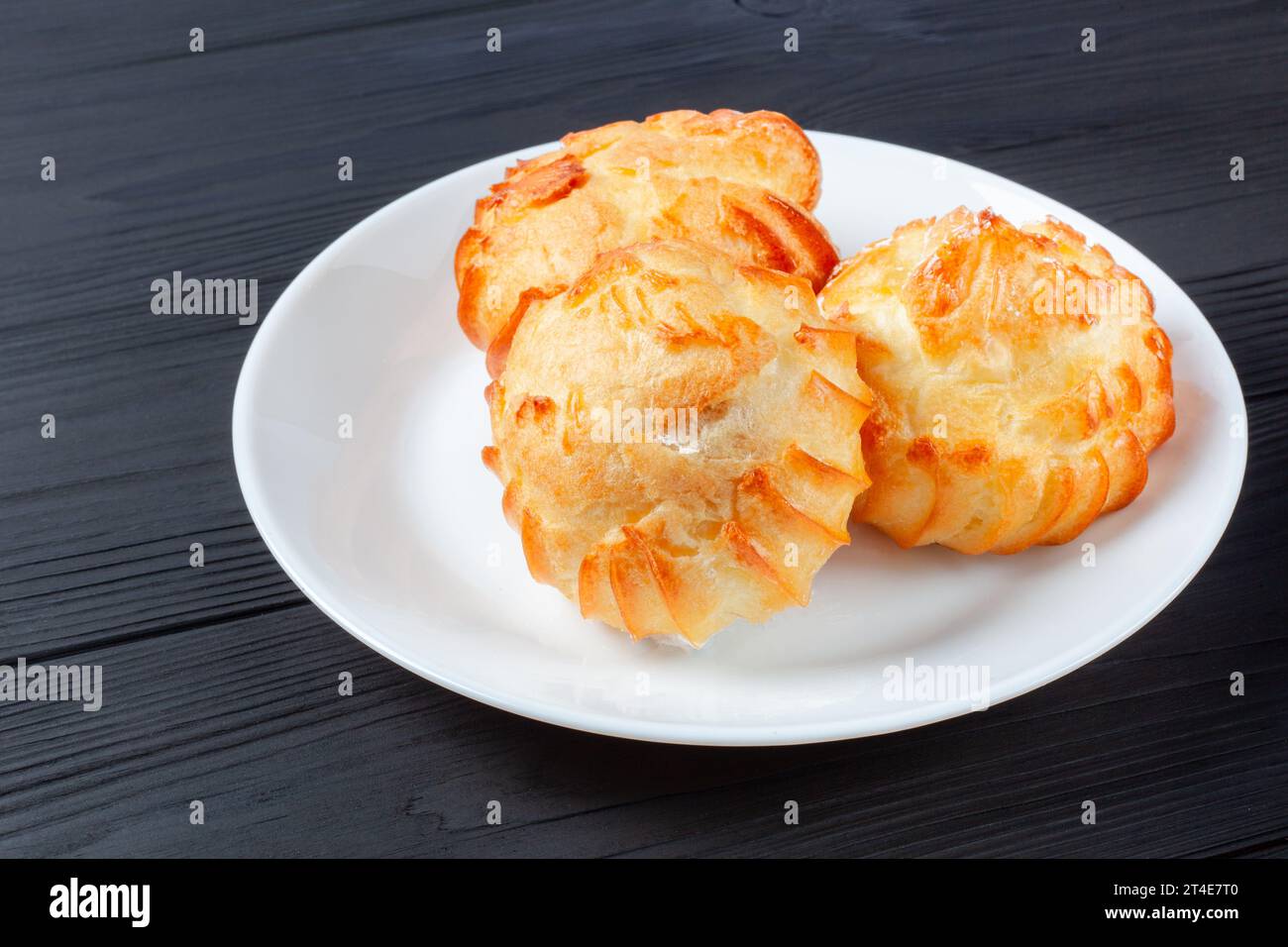 Profiterole dorate ripiene di panna, servite su un piatto bianco su un tavolo scuro. un delizioso abbinamento di dessert per ogni occasione. Foto Stock