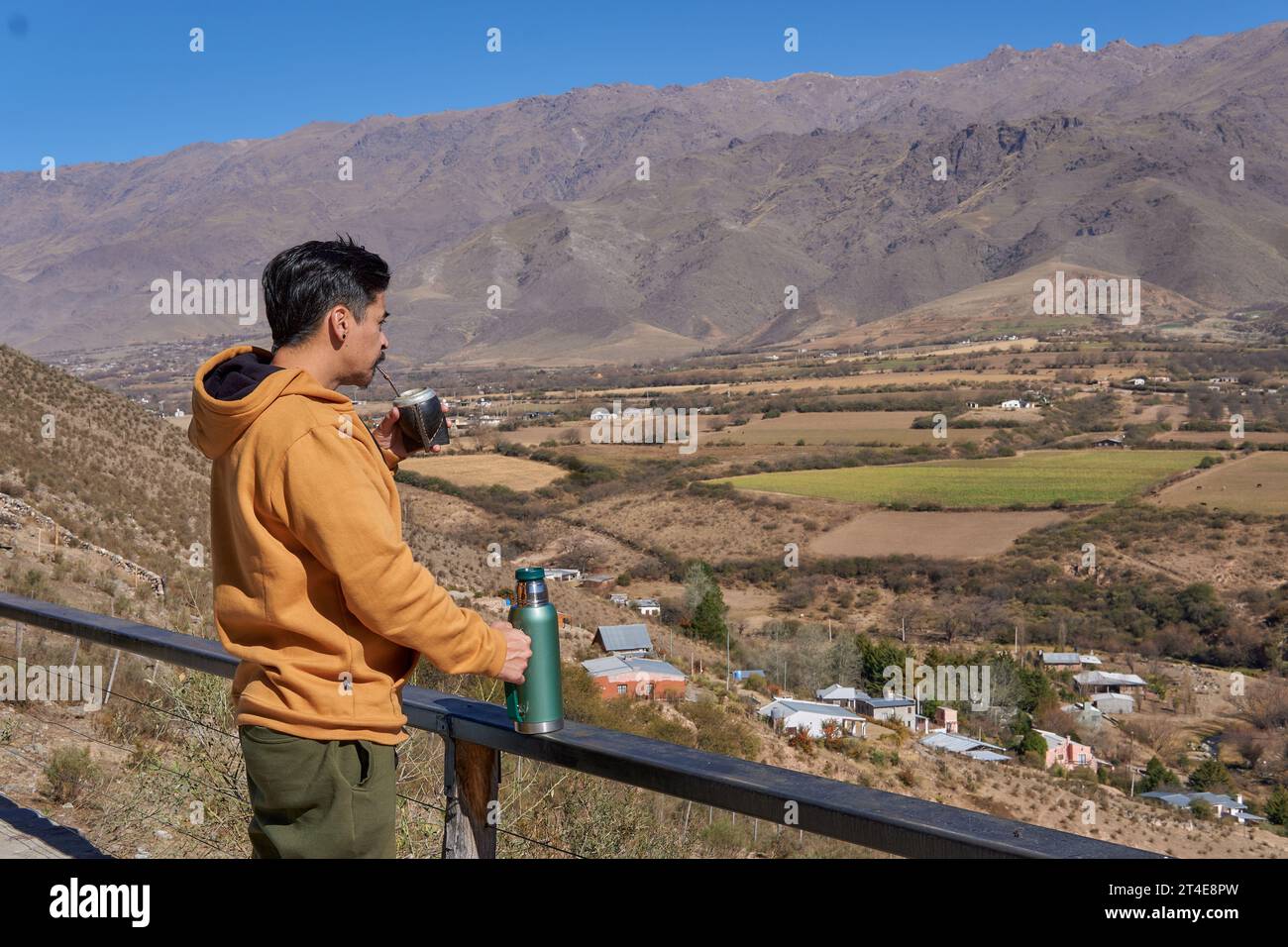 Uomo latino vestito con una felpa color senape, compagno di bevute che guarda il paesaggio da un balcone a tafi del Valle, Tucuman, Argentina. Rilassati Foto Stock