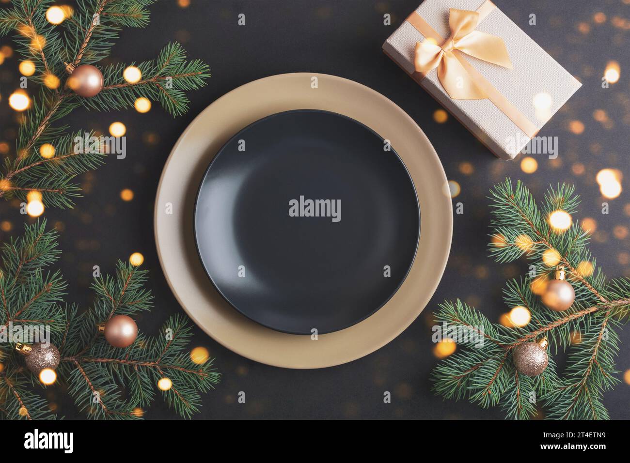 Elegante tavolo con rami di abete e palline di Natale, piatto nero e confezione regalo su sfondo nero. Concetto di Natale. Vista dall'alto, base piatta. Foto Stock