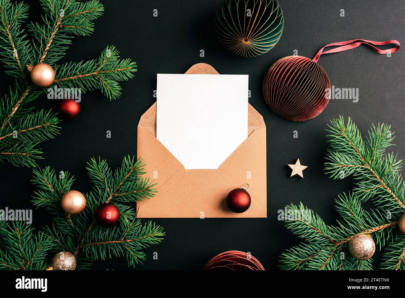 Busta con scheda vuota e rami di abete con palline di Natale su sfondo nero. Concetto di Natale. Vista dall'alto, base piatta, mockup. Foto Stock
