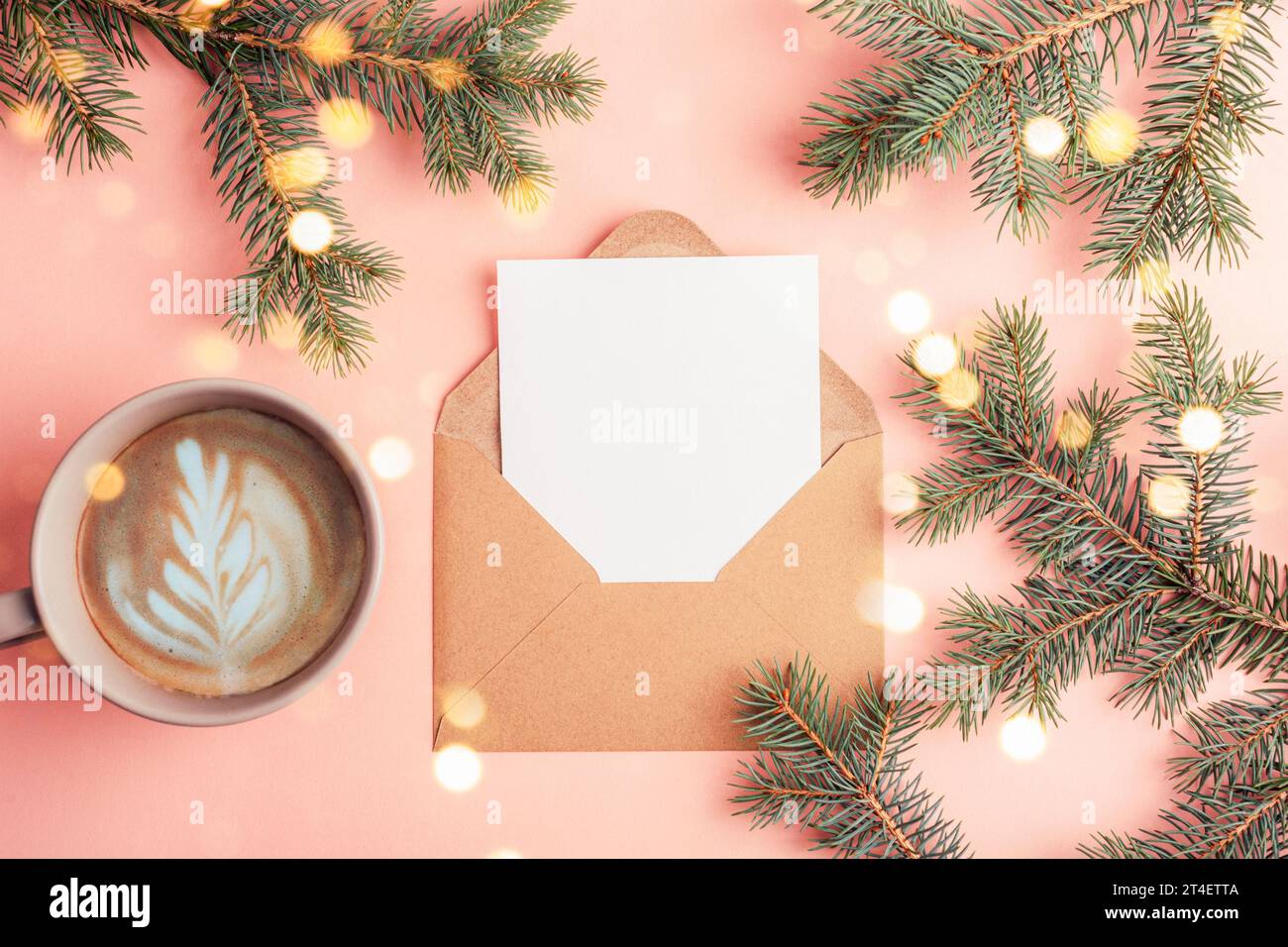 Busta con cartolina vuota, tazza da caffè e rami di abete con luci natalizie sul tavolo rosa. Concetto di Natale. Vista dall'alto, base piatta, mockup. Foto Stock