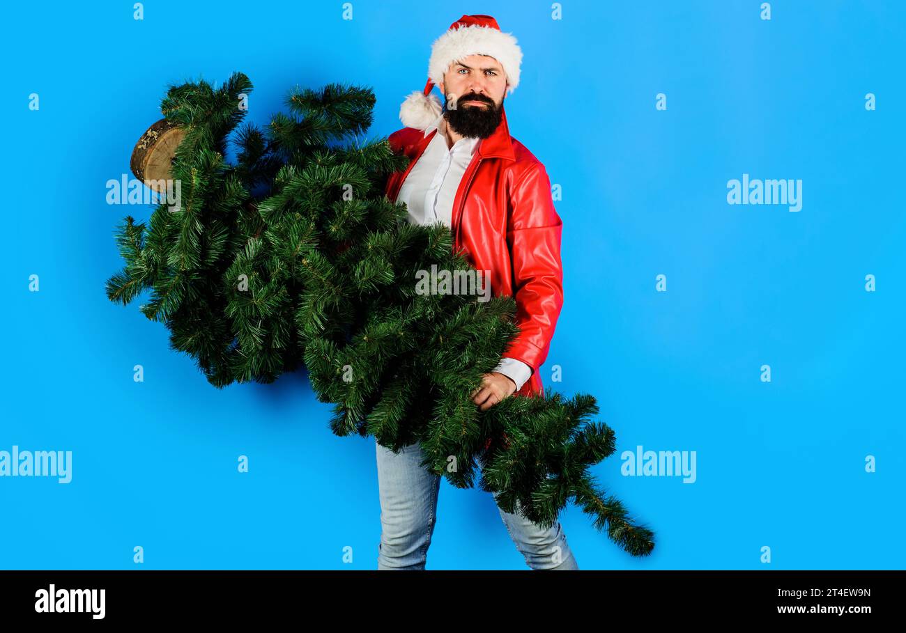 Uomo d'affari barbuto a Babbo Natale che porta l'albero di Natale. Consegna Babbo Natale in giacca di pelle rossa con abete. Natale e Capodanno. Preparazione Foto Stock