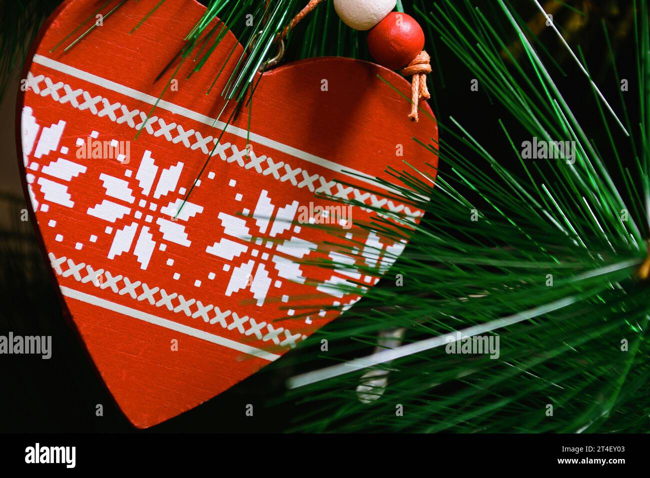 Giocattolo di Natale a forma di cuore circondato da aghi verdi provenienti da un albero di Natale artificiale Foto Stock