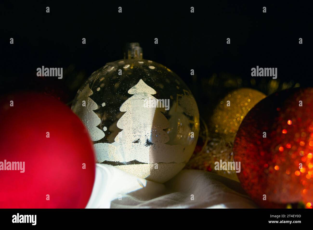 L'ombra cade su un giocattolo traslucido dell'albero di Natale circondato da altre decorazioni dell'albero di Natale su uno sfondo nero Foto Stock