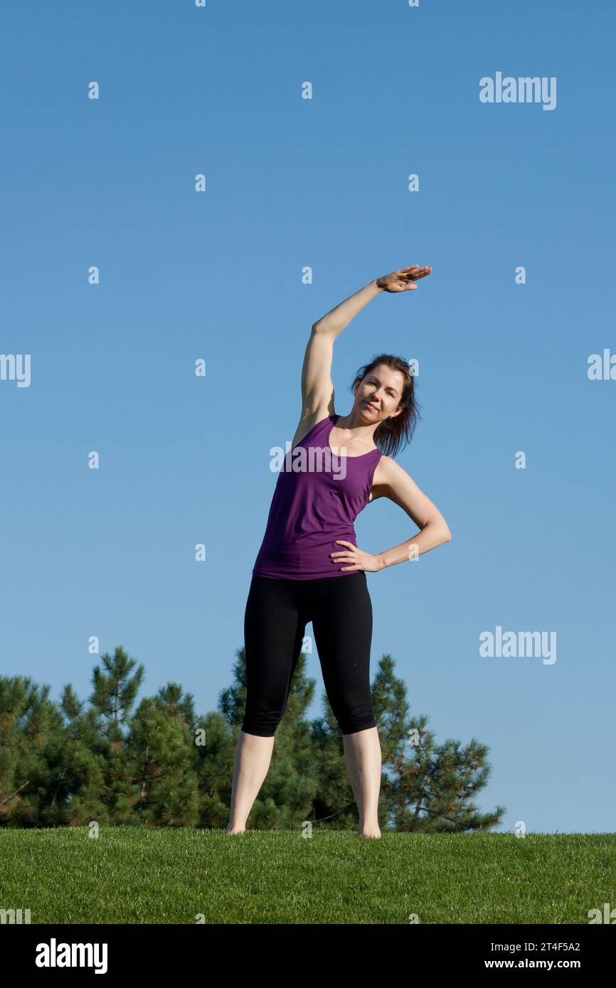 Giovane donna atletica che si riscalda prima di allenarsi nel parco, sfondo blu cielo. Bella donna con figure atletiche che pratica yoga, Pilates, Foto Stock