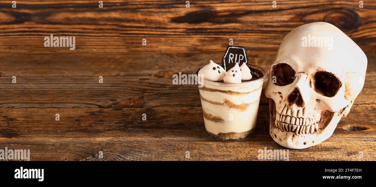 Tazza di plastica con delizioso tiramisù e teschio per festeggiare Halloween su sfondo di legno con spazio per il testo Foto Stock