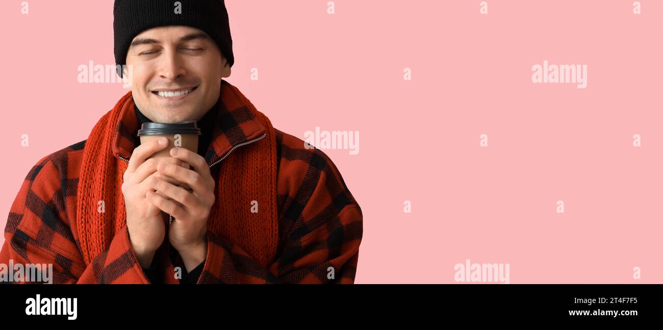 Giovane uomo felice in abiti invernali e con una tazza di caffè caldo su sfondo rosa Foto Stock