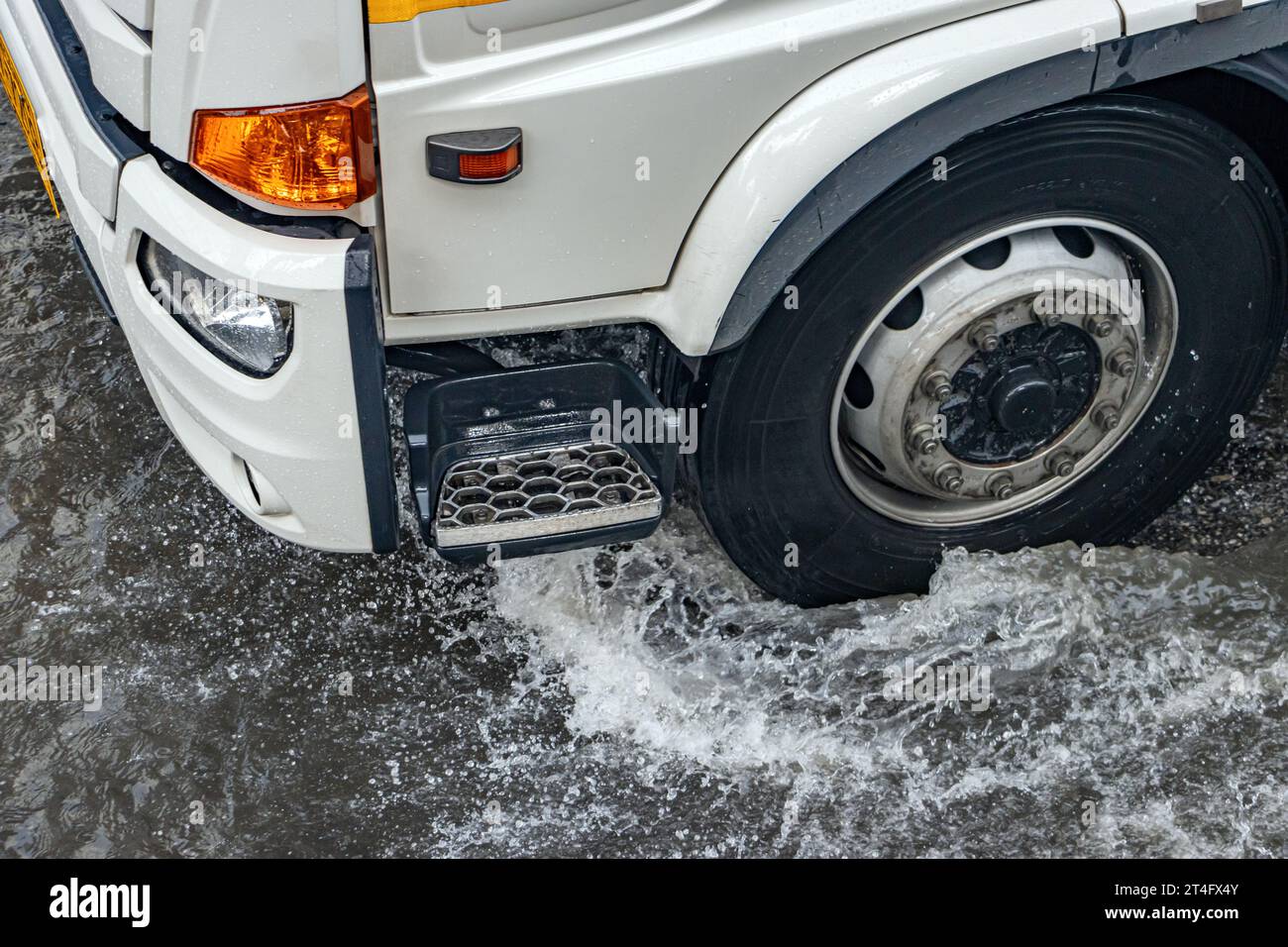 Lo sguardo dettagliato sulla ruota del camion che attraversa una strada allagata sotto la pioggia Foto Stock