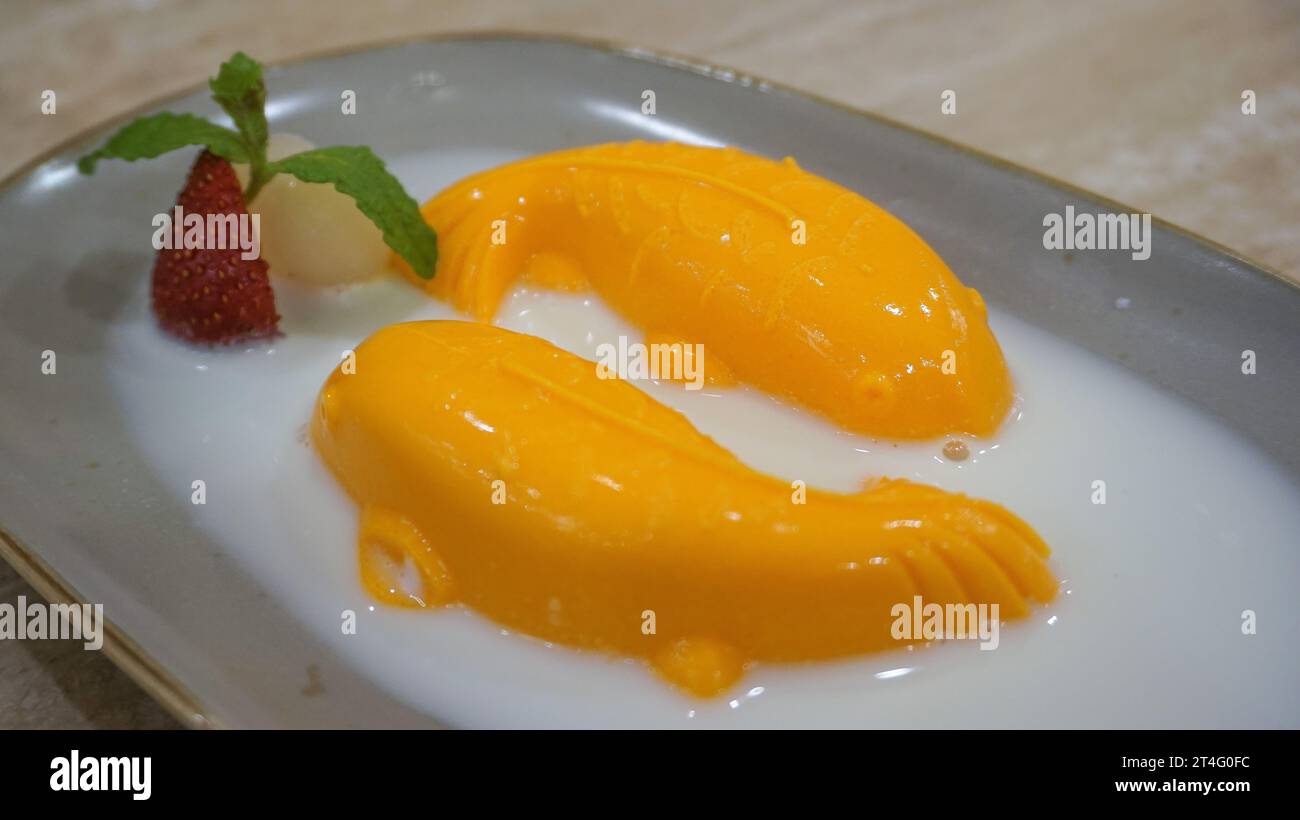Budino di mango a forma di pesce con condimenti leciti, fragole e foglie di menta su un piatto bianco Foto Stock