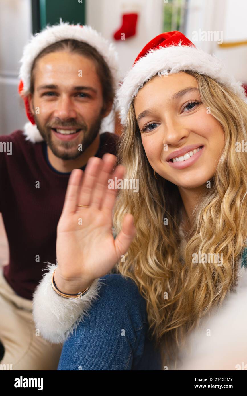 Felice coppia caucasica nei cappelli di natale con videochiamata, sorridendo e salutando a casa Foto Stock