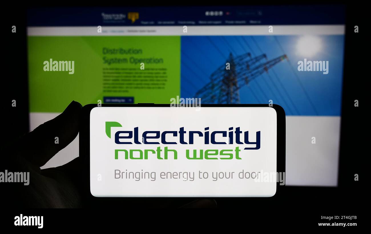 Persona che possiede uno smartphone con il logo della società energetica britannica Electricity North West Limited davanti al sito Web. Concentrarsi sul display del telefono. Foto Stock