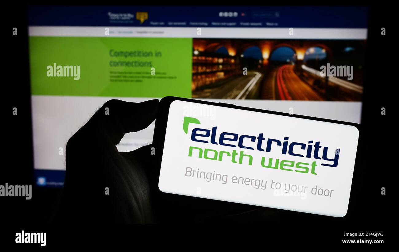 Persona in possesso di un cellulare con il logo della società energetica britannica Electricity North West Limited davanti alla pagina Web dell'azienda. Concentrarsi sul display del telefono. Foto Stock