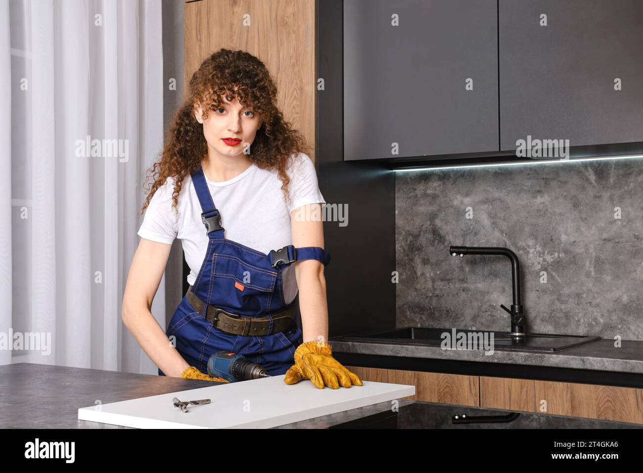 Donna che trapana un foro in un pannello di truciolato in cucina Foto Stock