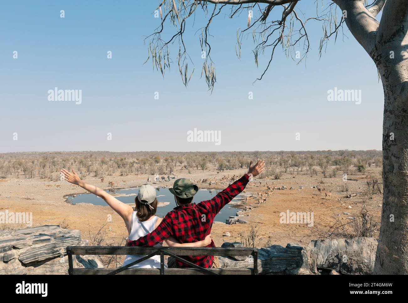 Vista posteriore di giovani coppie con le mani in alto che osservano gli animali della savana africana, del parco nazionale di Etosha, della Namibia Foto Stock