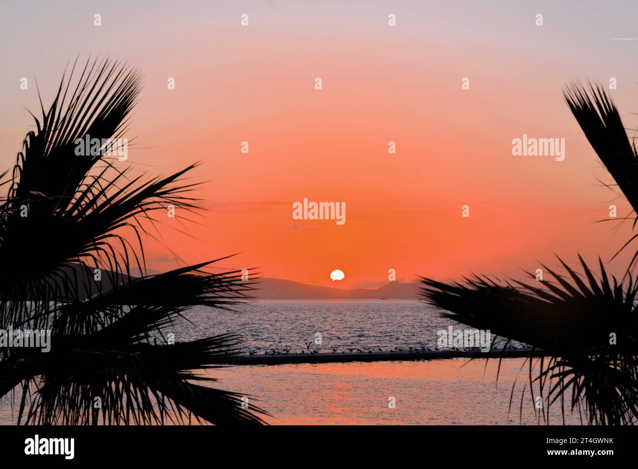 Cielo cremisi e sole a sfera al tramonto sul mare dietro le colline Foto Stock