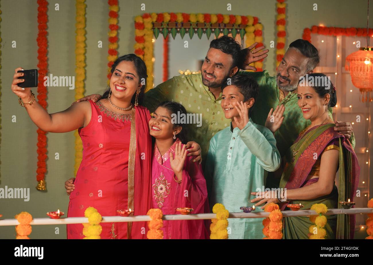 Gruppo di membri della famiglia indiana che effettua videochiamate sul cellulare per i desideri o i saluti di diwali durante le celebrazioni natalizie a casa - concetto di Foto Stock