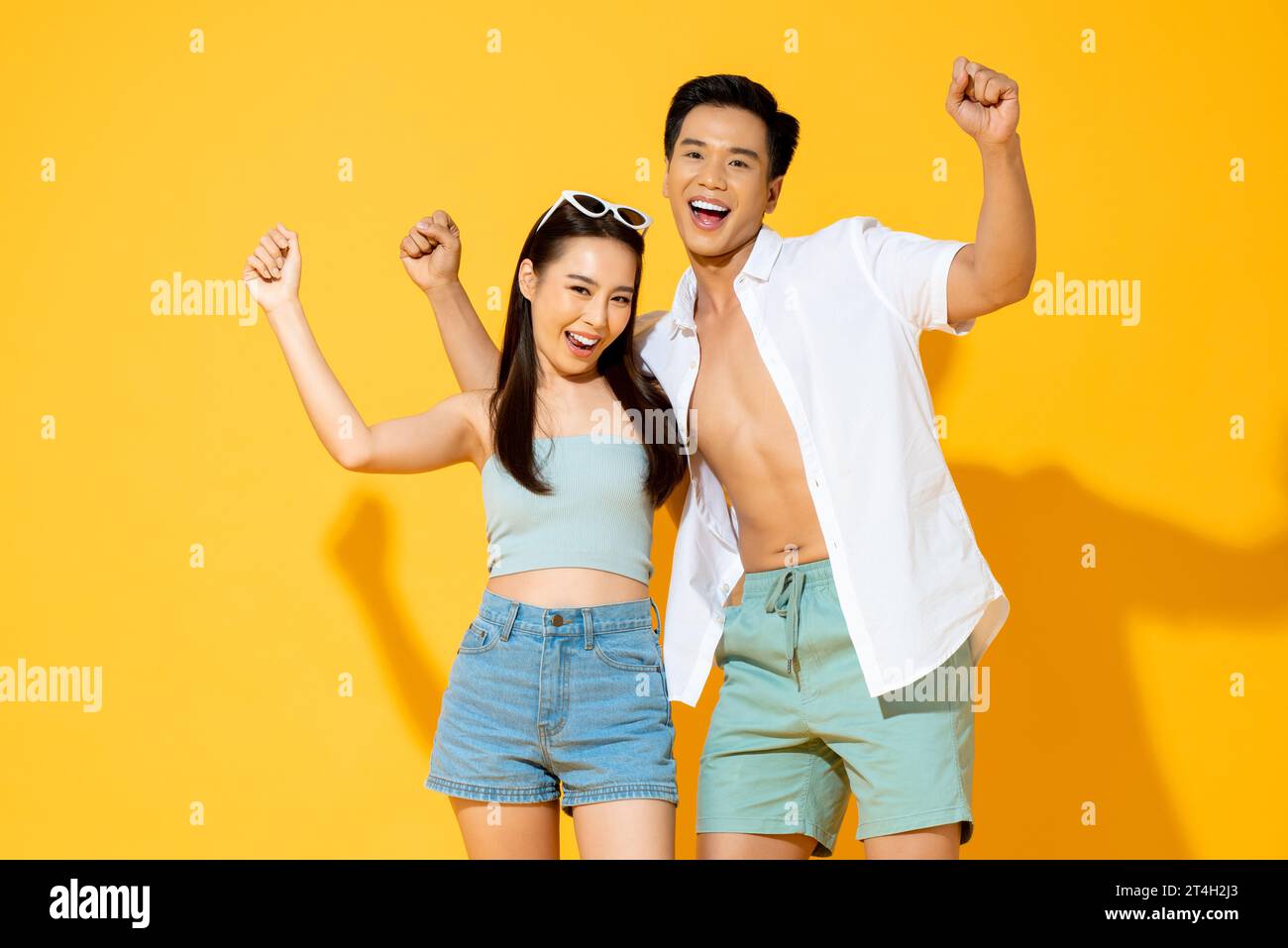 Eccitante coppia turistica asiatica in abiti estivi sorridenti e rialzanti con sfondo isolato di colore giallo Foto Stock