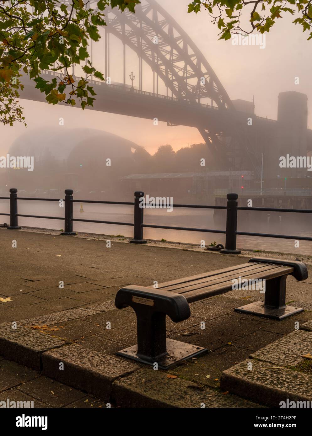 Ponte Tyne in una nebbiosa mattinata autunnale incorniciata da panchina e foglie autunnali Foto Stock