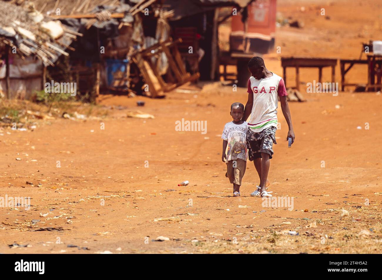 Un adulto e un bambino passeggiano davanti a una fila di baracche in legno rustico ad Abidjan, Costa d'Avorio Foto Stock